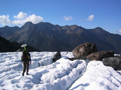 This image depicts a ranger carrying scientific equipment over a glacier.