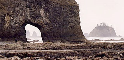 offshore islands in fog are beyond eroded arch in rock cliff in front