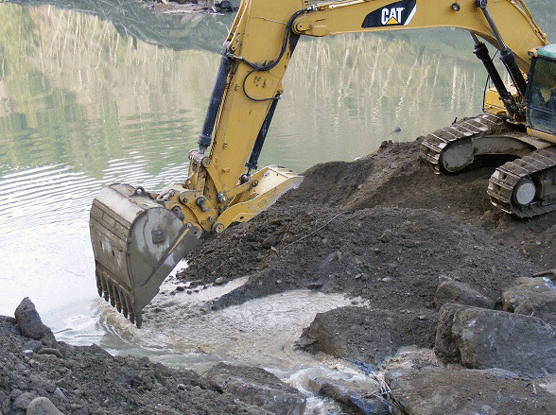 yellow excavator working alongside river