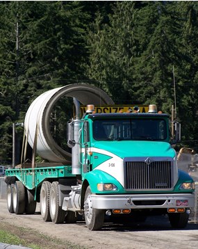 turquoise flatbed truck carrying large concrete cylinder