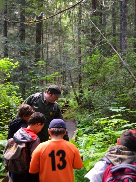 Park Ranger and young students observing plants on a forest trail.