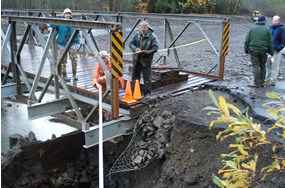 people standing on bridge; bridge shows damage with missing pavement and roadbed