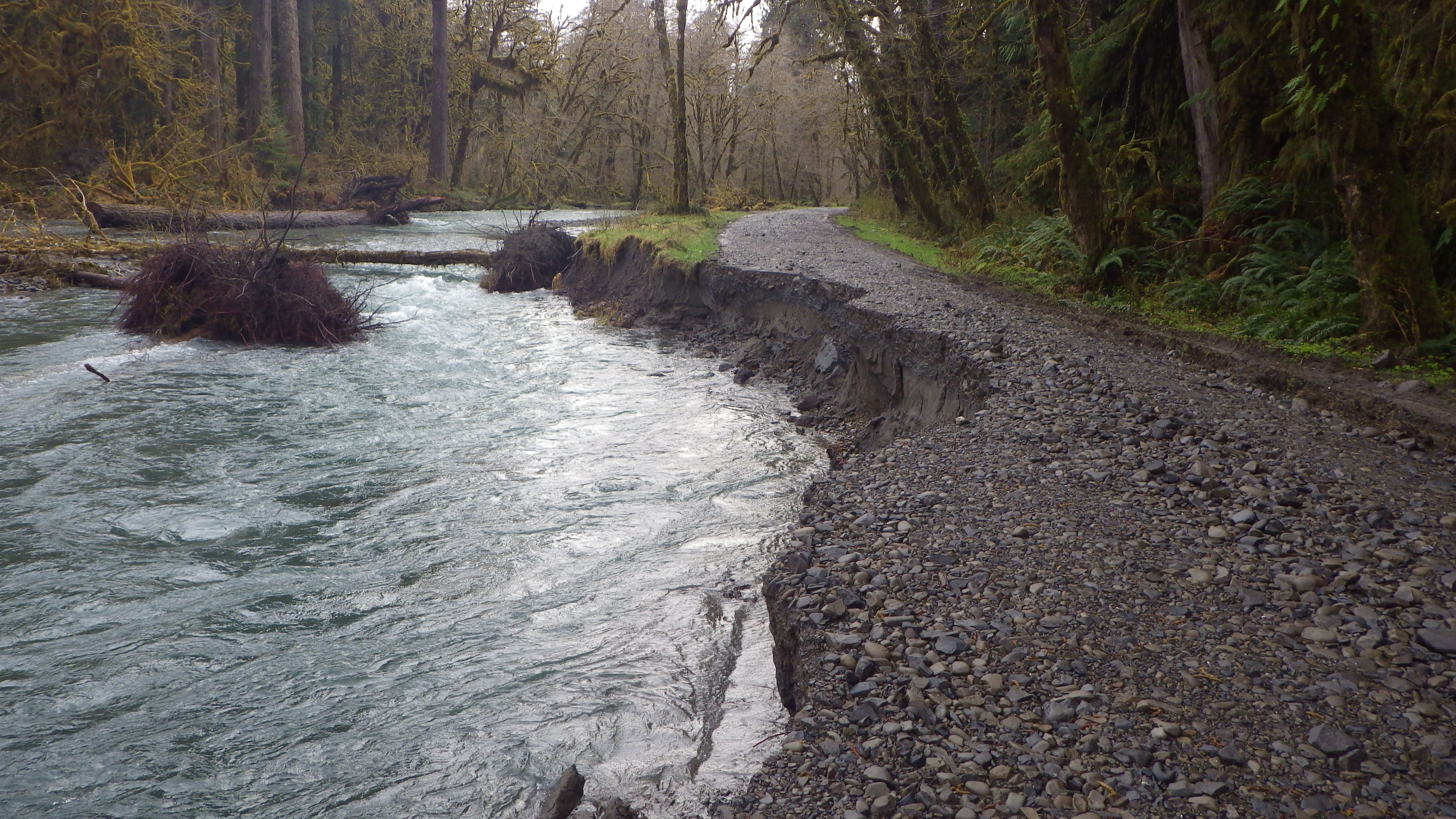 Gravel road washed out along a flooding river.