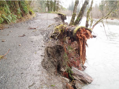 one-lane paved road next to a river; outside edge of road missing