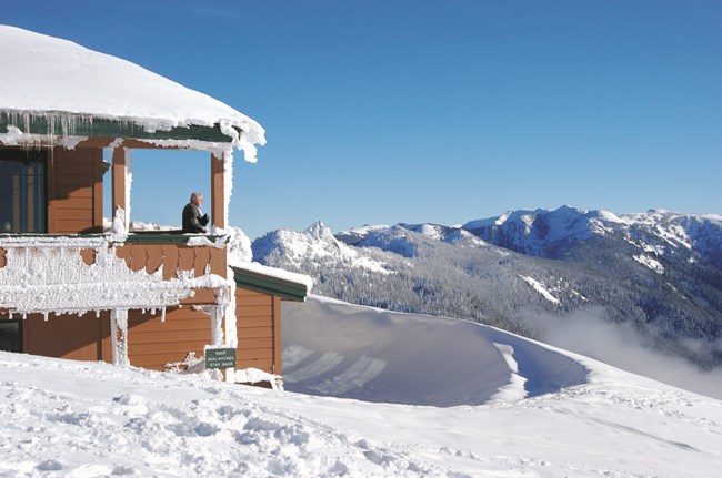 A building covered in snow with snowy mountains in the background.