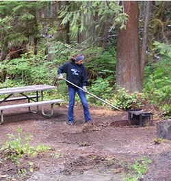 young woman raking near picnic table and fire grate