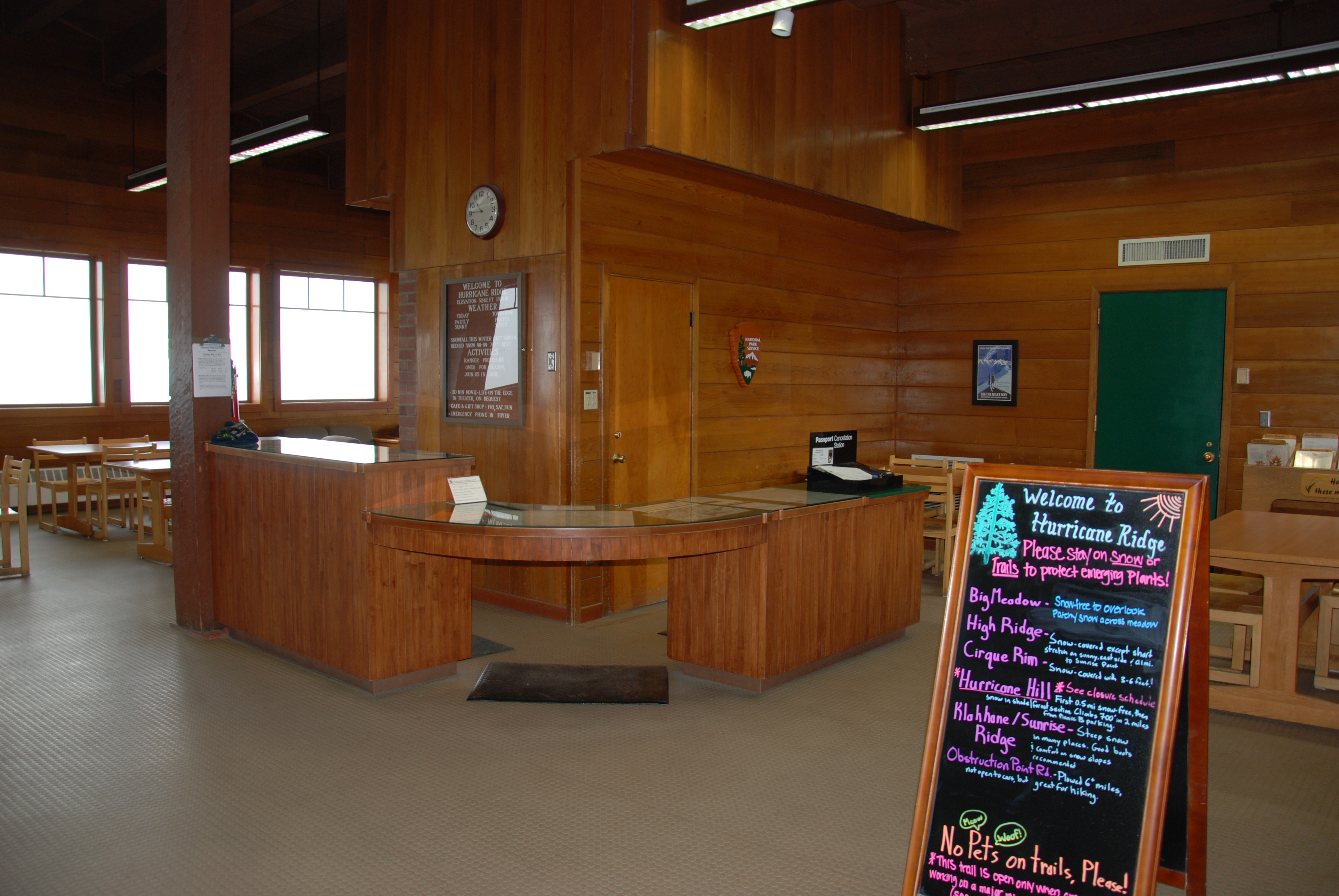 Interior of a wood building, with a wrap-around desk, information boards, windows, chairs and tables.