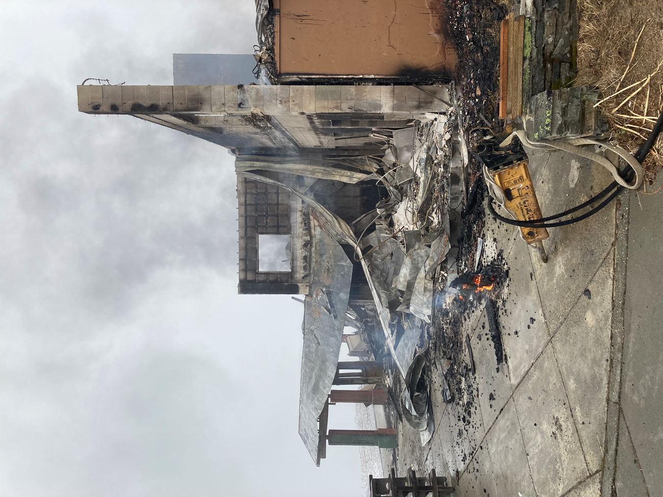 The smoking remains of a burned building, with some coals still glowing in part of the floor.