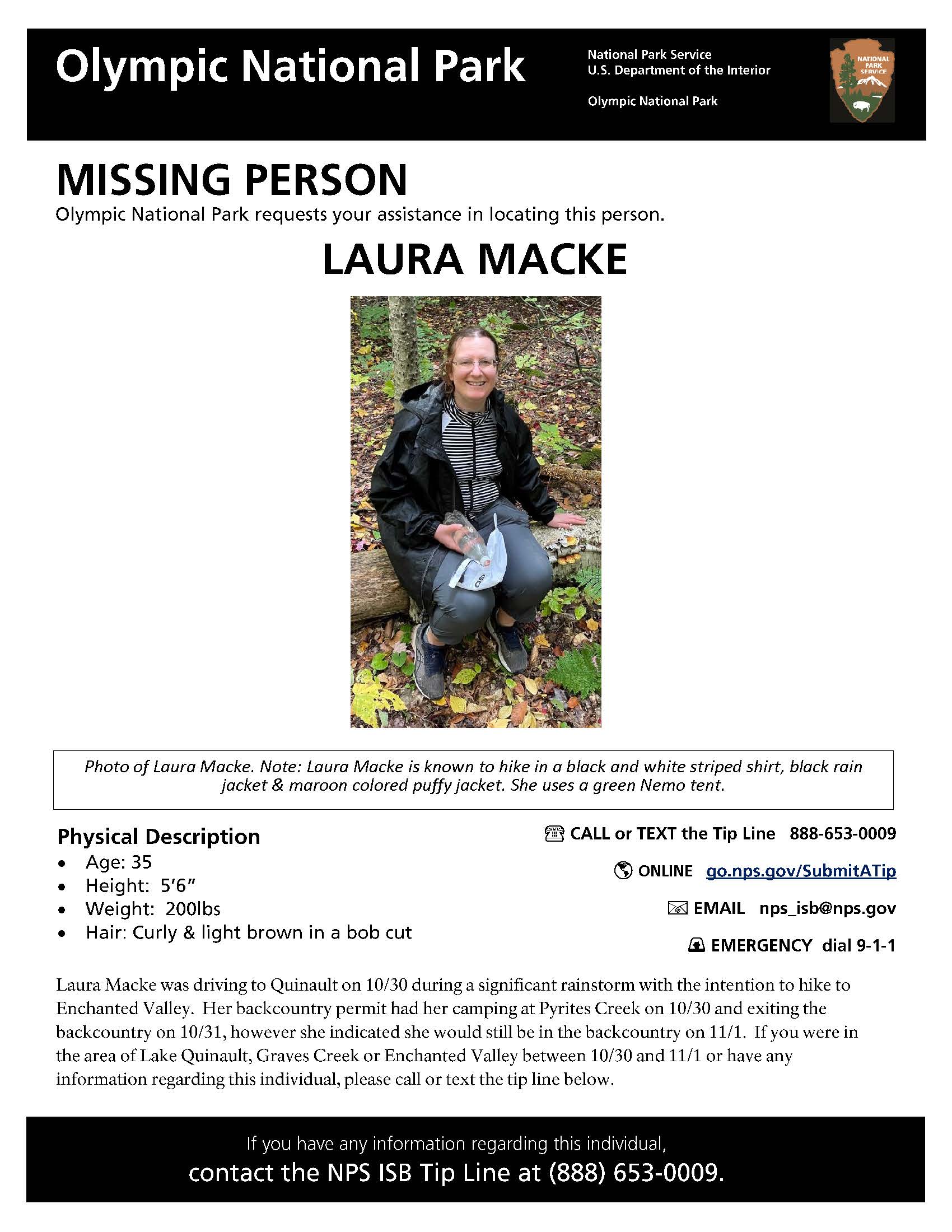 Missing Person Poster_Olympic_Laura Macke Laura Macke sits on a log in a forested area smiling at the camera. She is wearing a black jacket, black and white striped shirt, gray pants and gray shoes. She has light skin, brown hair that is pulled back and wears glasses.