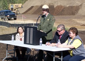 uniformed ranger speaking at outdoor podium, flanked by three other people