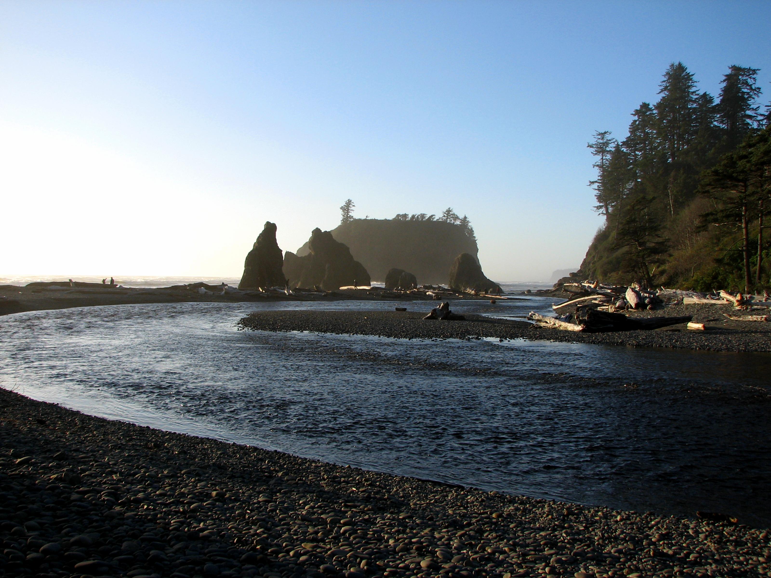 Morning at Ruby Beach, with a large sea stack, the blue Pacific Ocean, and a rocky beach covered with driftwood.