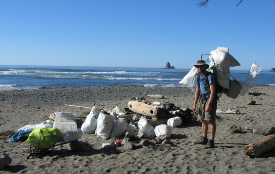 man with backpack standing near many filled garbage bags on ocean beach man with backpack standing near many filled garbage bags on ocean beach