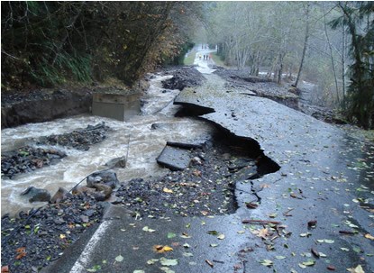 brown water flows alongside a damaged road