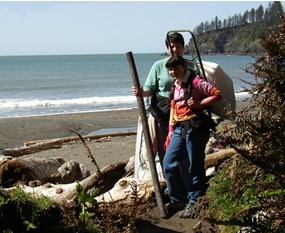 two people with trash bags with ocean in background
