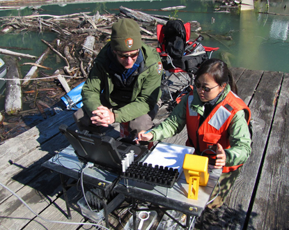 Two fisheries biologists, Sam Brenkman of the National Park Service and Meimei Li of the U.S. Fish and Wildlife Service, input tagging information to a computer on the dock at Lake Mills.