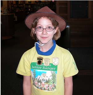 girl wearing a ranger hat and yellow shirt with three junior ranger badges