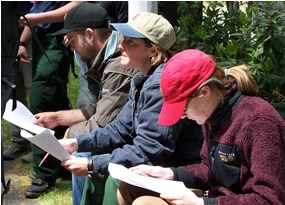 three people outdoors, each holding papers