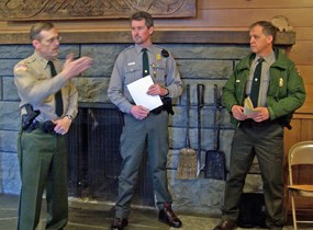 three uniformed men standing before stone fireplace
