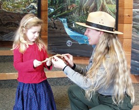young girl with red shirt looking at an object held by female ranger with long blond hair