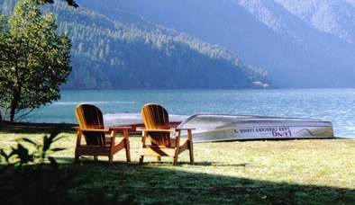 two wooden chairs near lakeshore; rowboats along shore