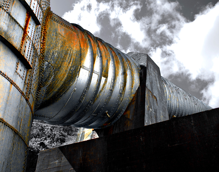 Looking up at the intake which feeds the surge tank at the Elwha Dam. Rust spots on the metal and clouds in the background.