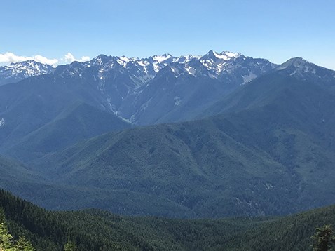 Unobstructed view looking across a wide river valley. On the other side of the river valley lies rugged, snow-capped mountains.