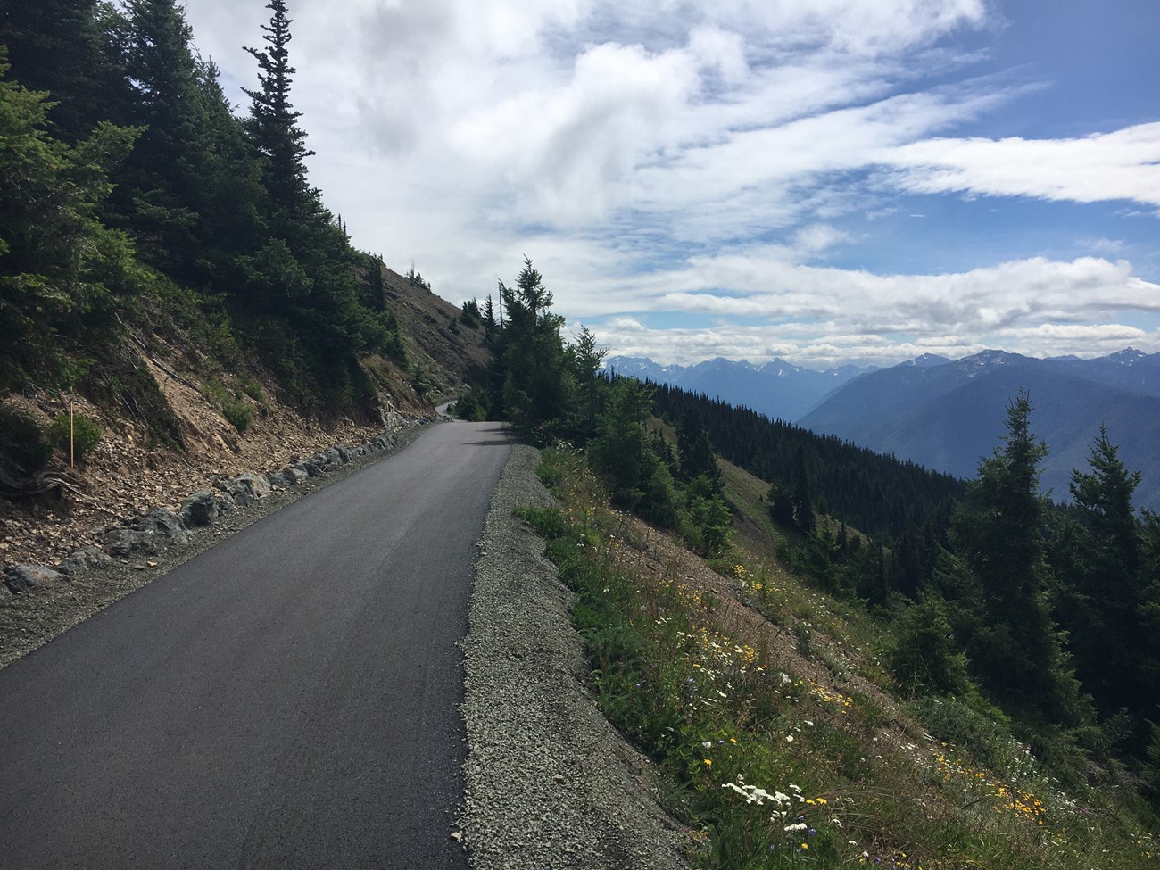 A paved trail along a hillside with mountains in the distance