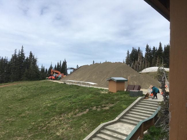 Construction equipment and pile of sand near an open grassy area and sidewalk.