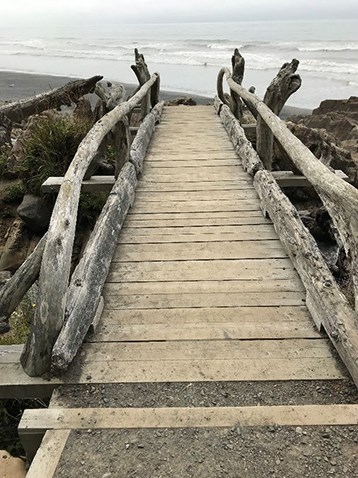 A wooden bridge improvised with driftwood, which is nailed in as handrails on each side.