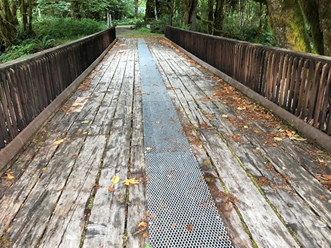 A wide, mostly wooden bridge with wooden railings. A narrow metal grate runs the span of the bridge.