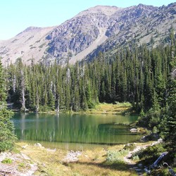Royal Lake, with greenish blue water, surrounded by trees and backdropped by a mountain ridge.