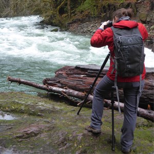 Photographer using a tripod to capture a photo of a river rapids.