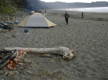 A small fire near a tent on the beach.
