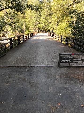 A wide, paved bridge partially blocked with a gate that reads "Pedestrians and authorized vehicles only beyond this point."