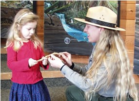 A uniformed Park Ranger kneeling down to talk with a small child.