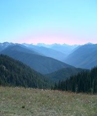 A view of sky and mountains from atop a mountain meadow during the summer