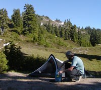 Hiker at wilderness campsite storing food in bear canister.