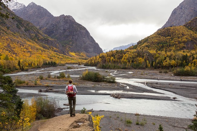 Hiker viewing fall colors near river.