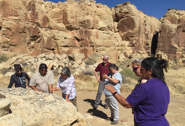 NPS staff and tribal members talking around rocks in a desert
