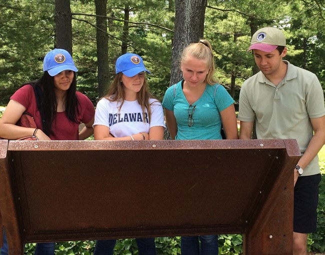 Four students gather around a wayside sign to read.