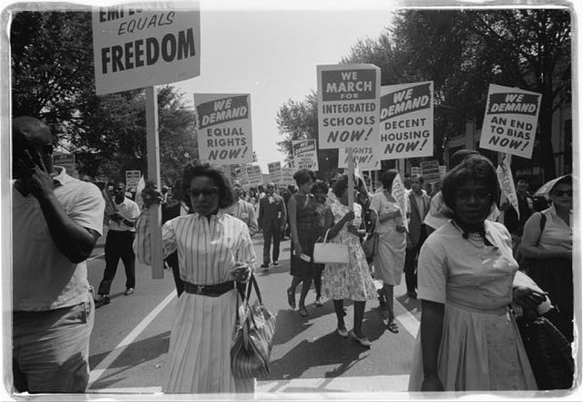 a procession of African Americans carrying signs for equal rights, integrated schools, decent housing, and an end to bias.