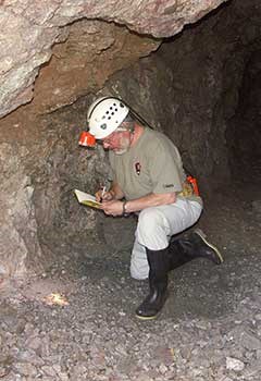 A man wearing a helmet and kneeling, documents abandoned mine features.