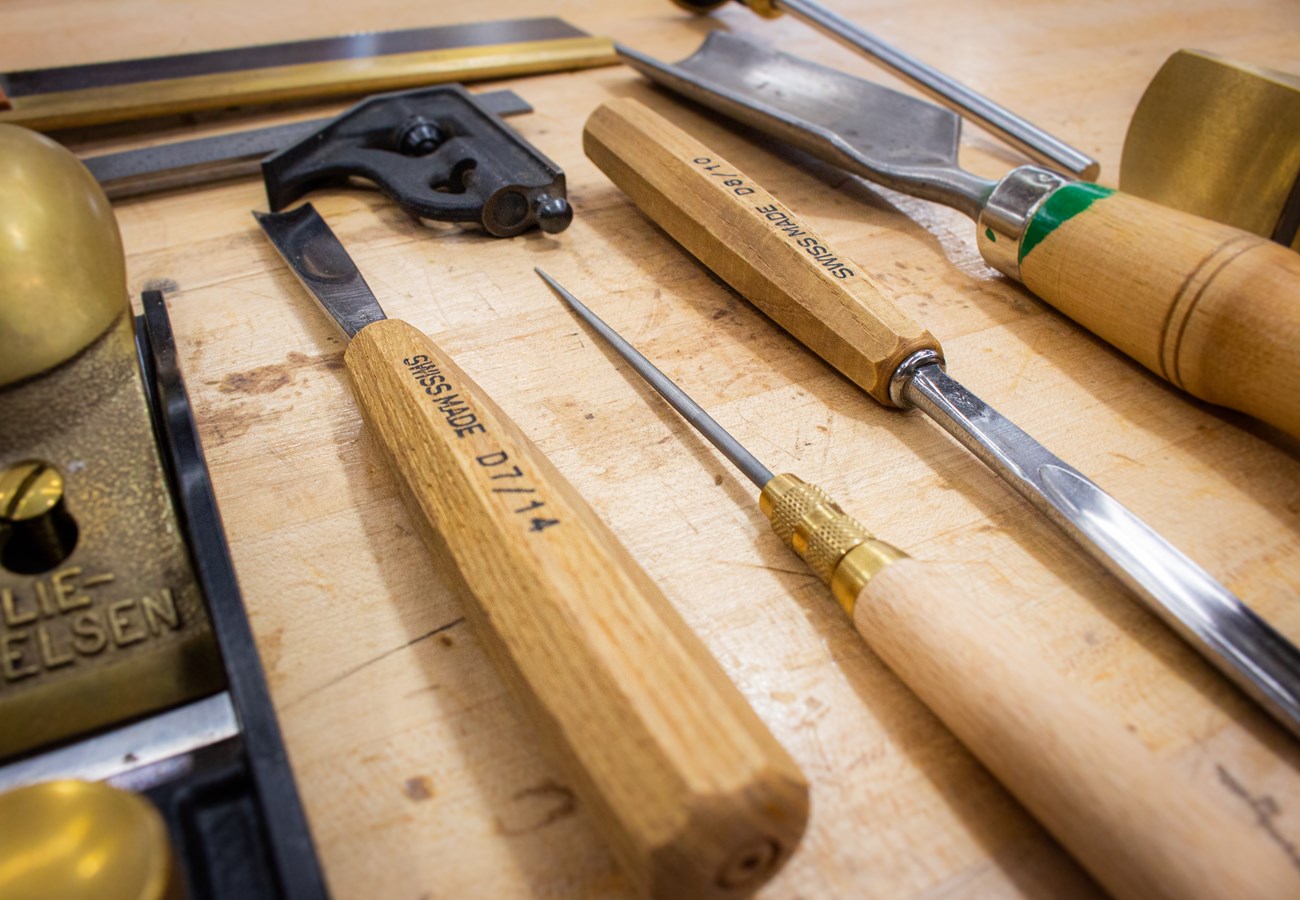 Various woodworking chisels, hammers, and planes on a wood worktop.