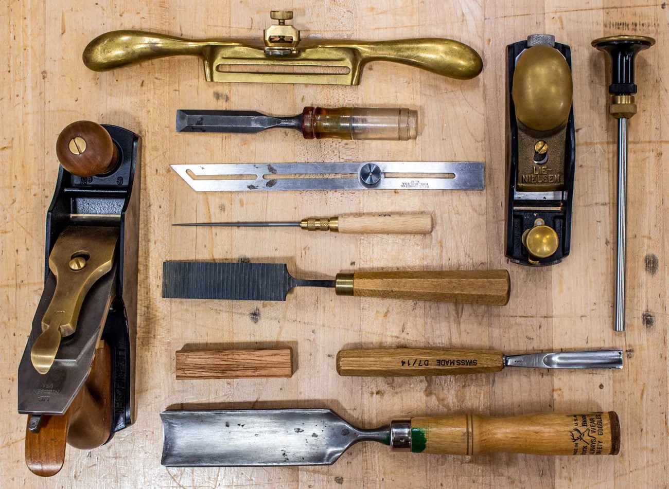 Various woodworking tools laid flat on a wooden table. Chisels, planers, rulers, and more.