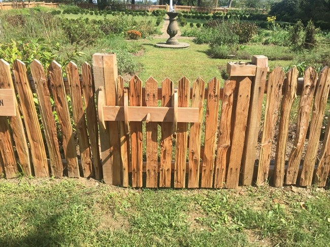 A brown painted fence with a fountain in the background