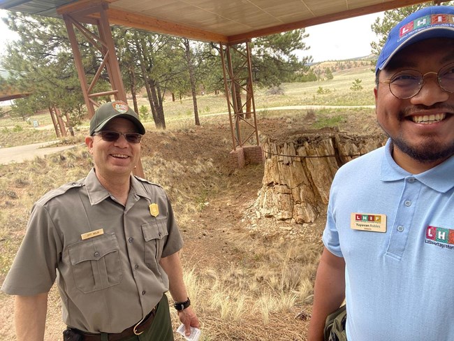 A male NPS employee in uniform stands next to a male intern wearing an LHIP polo, nametag, and hat