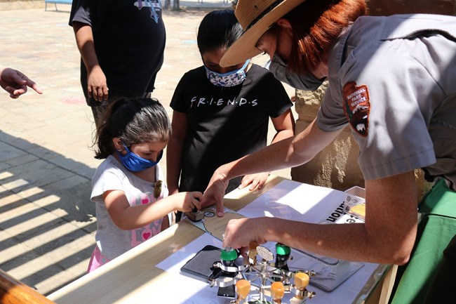 A woman in an NPS uniform helps a small girl stamp her Junior Ranger badge.