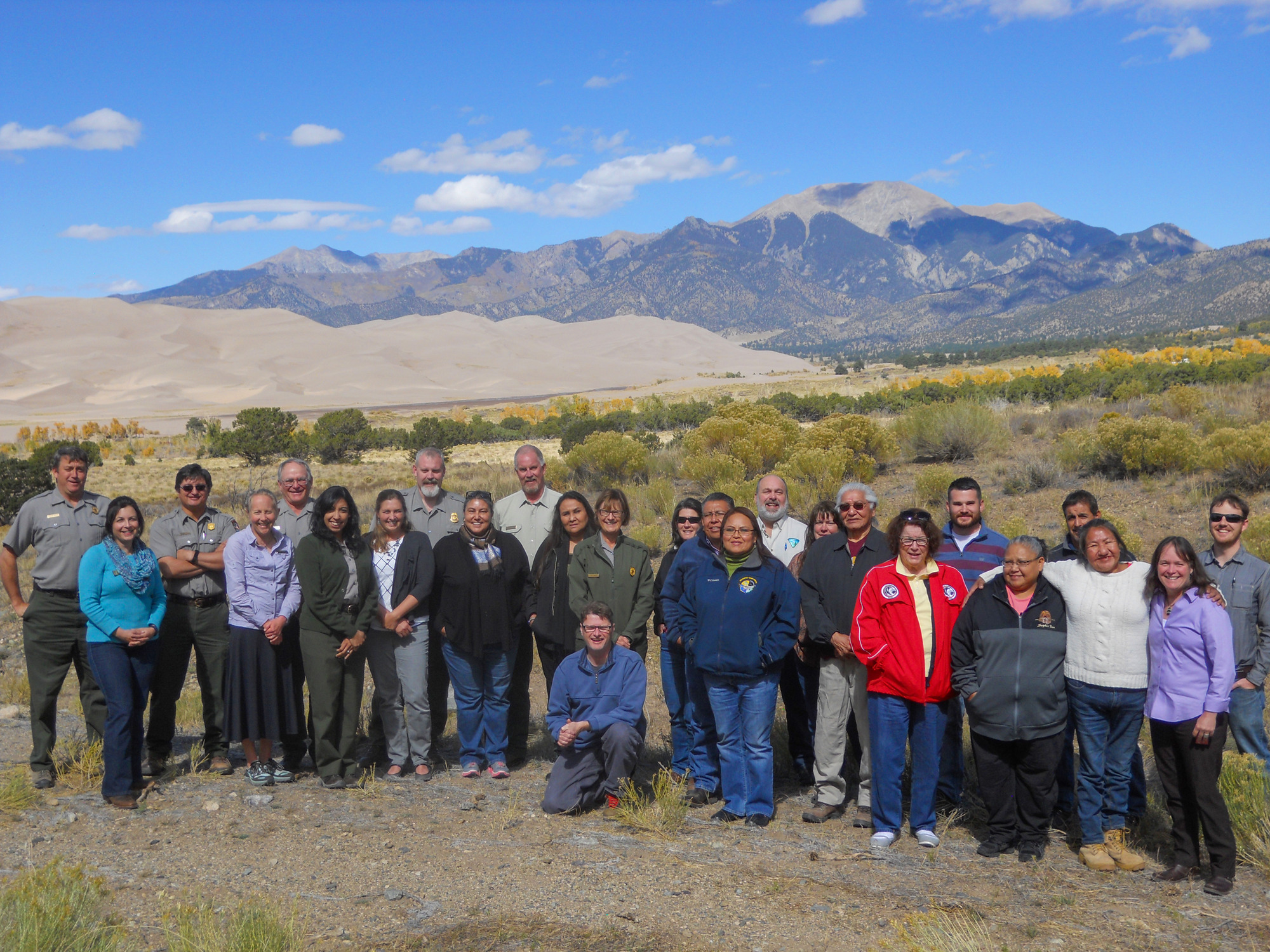 Representatives from the Southern Ute, Ute Tribe of Uinta and Ouray, Ute Mountain Ute, Jicarilla Apache, and Navajo tribes stand with Interior Department staff after a tribal consultation. In the background are the dunes and Sangre de Cristo Mountains. Representatives from the Southern Ute, Ute Tribe of Uinta and Ouray, Ute Mountain Ute, Jicarilla Apache, and Navajo tribes stand with Interior Department staff after a tribal consultation. In the background are the dunes and Sangre de Cristo Mountains.