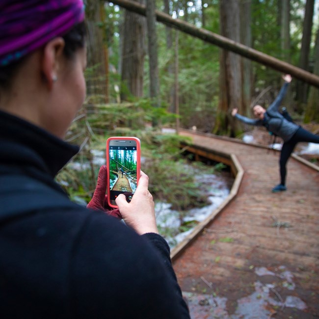 A woman poses for a photo while on a trail in a forest.