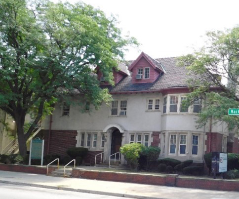 A three story building on an empty street with a tree on the left side.